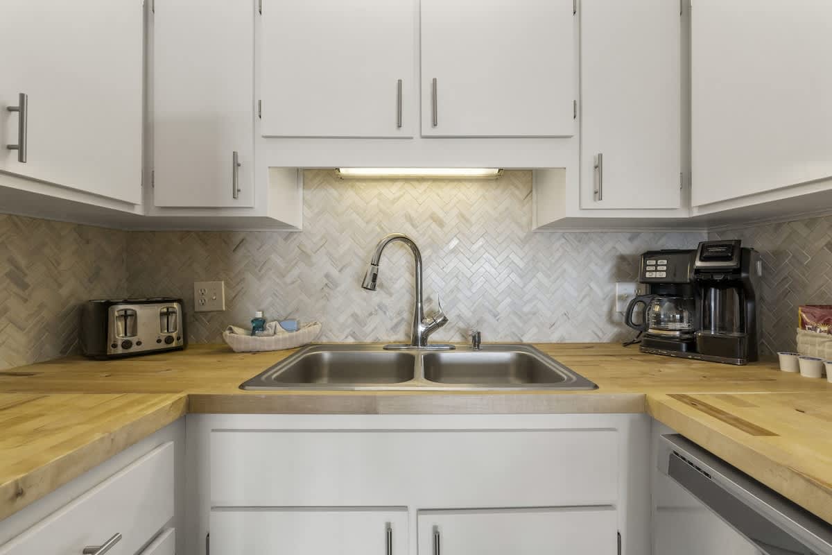 The Summit 1216 – Modern kitchen with double sink, herringbone backsplash, wooden countertops, toaster, and coffee maker.
