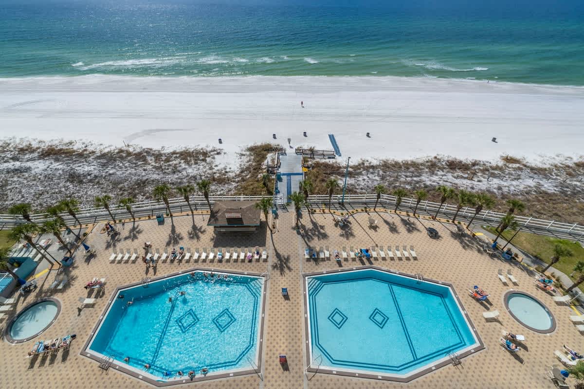 The Summit 1216 – Two swimming pools, beach access, and palm trees overlooking white sand and ocean.