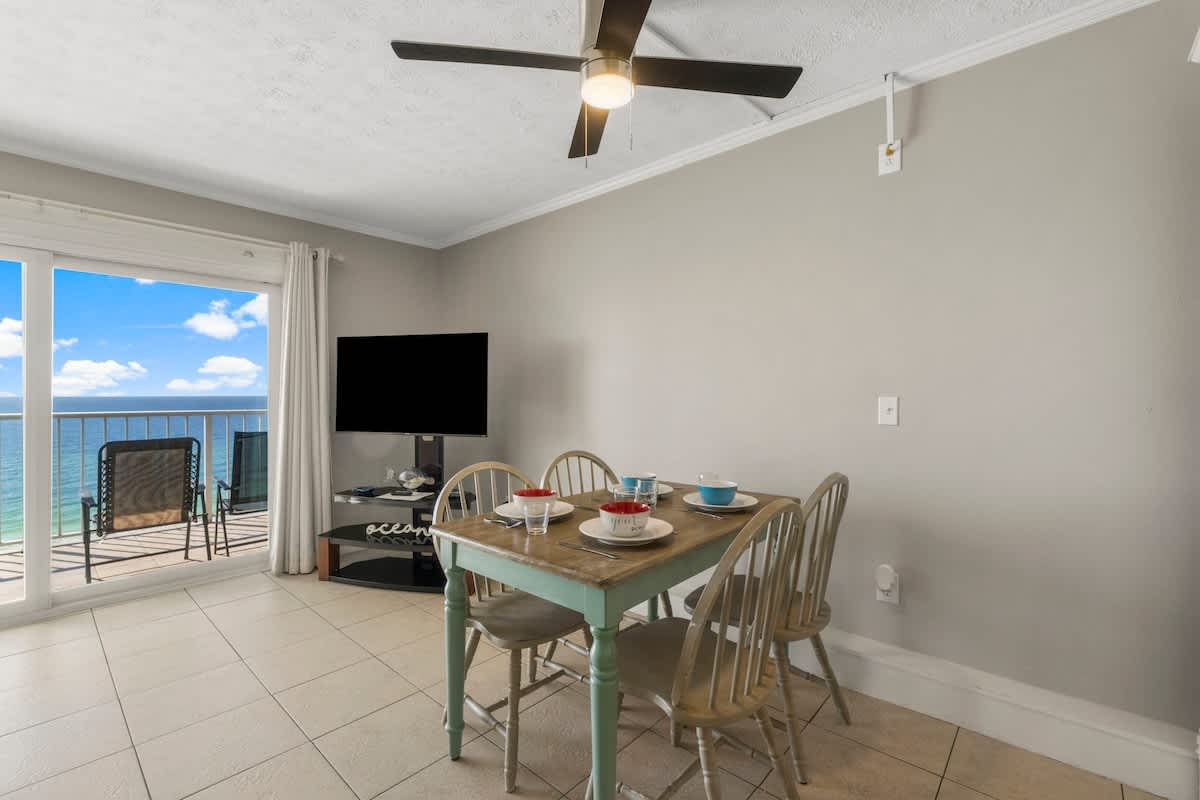 The Summit 1216 – Dining area with table set, TV, and view of the ocean through sliding glass doors.