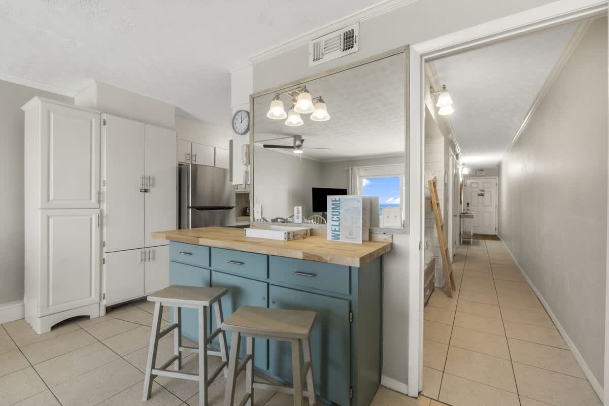 The Summit 1216 – Bright kitchen with blue cabinetry, wood countertop, bar stools, and hallway leading to a view of the outdoors.