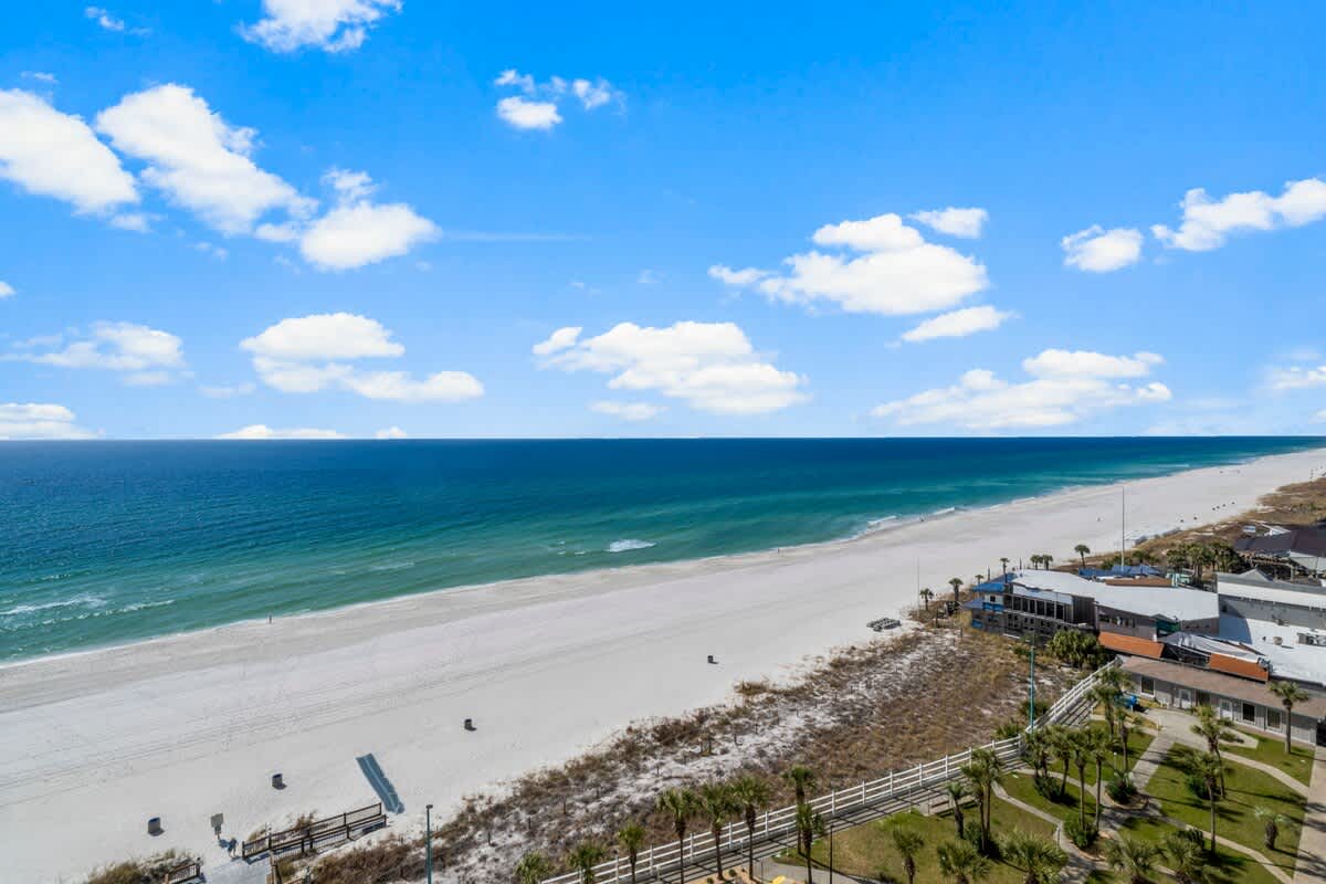 The Summit 1216 – Ocean view from a balcony overlooking a white sandy beach and green shoreline.