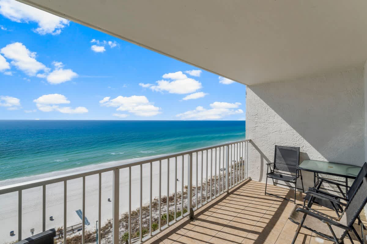The Summit 1216 – Balcony view with seating, overlooking the beach and ocean under a clear blue sky.