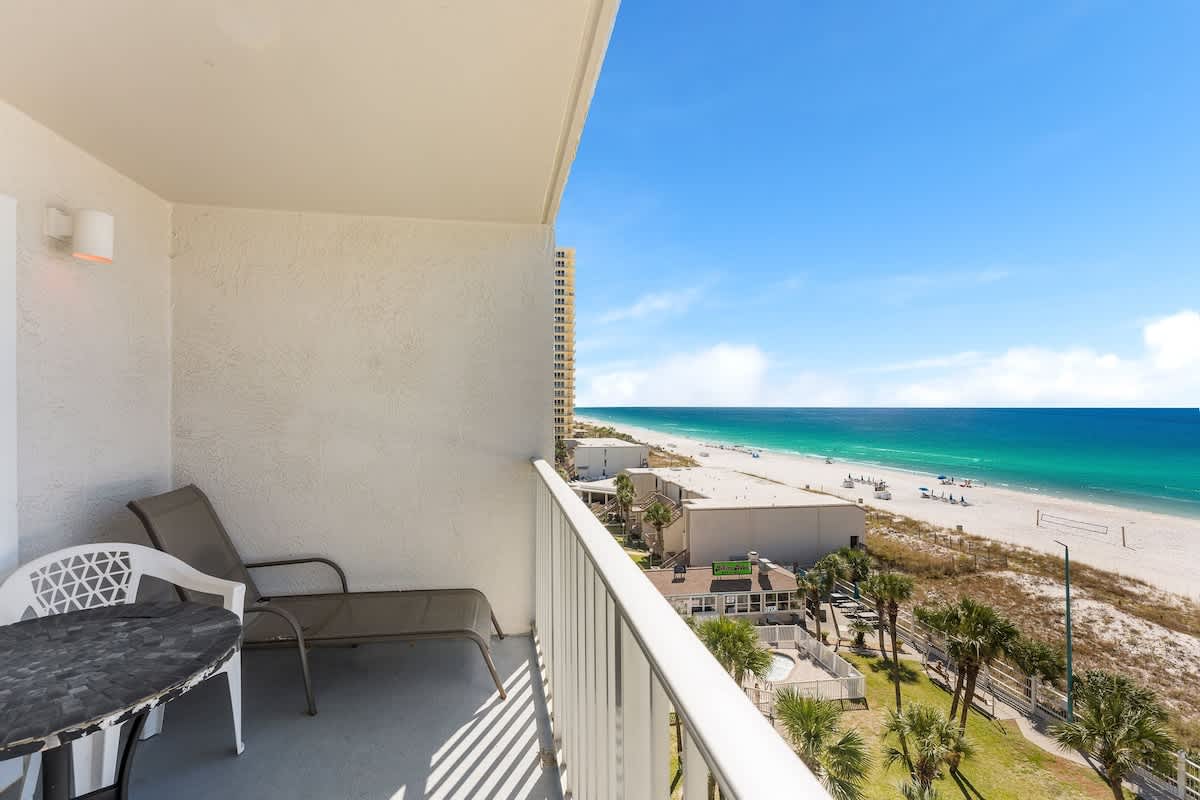 The Summit 726 – Balcony view of sandy beach, turquoise water, palm trees, and outdoor seating area.