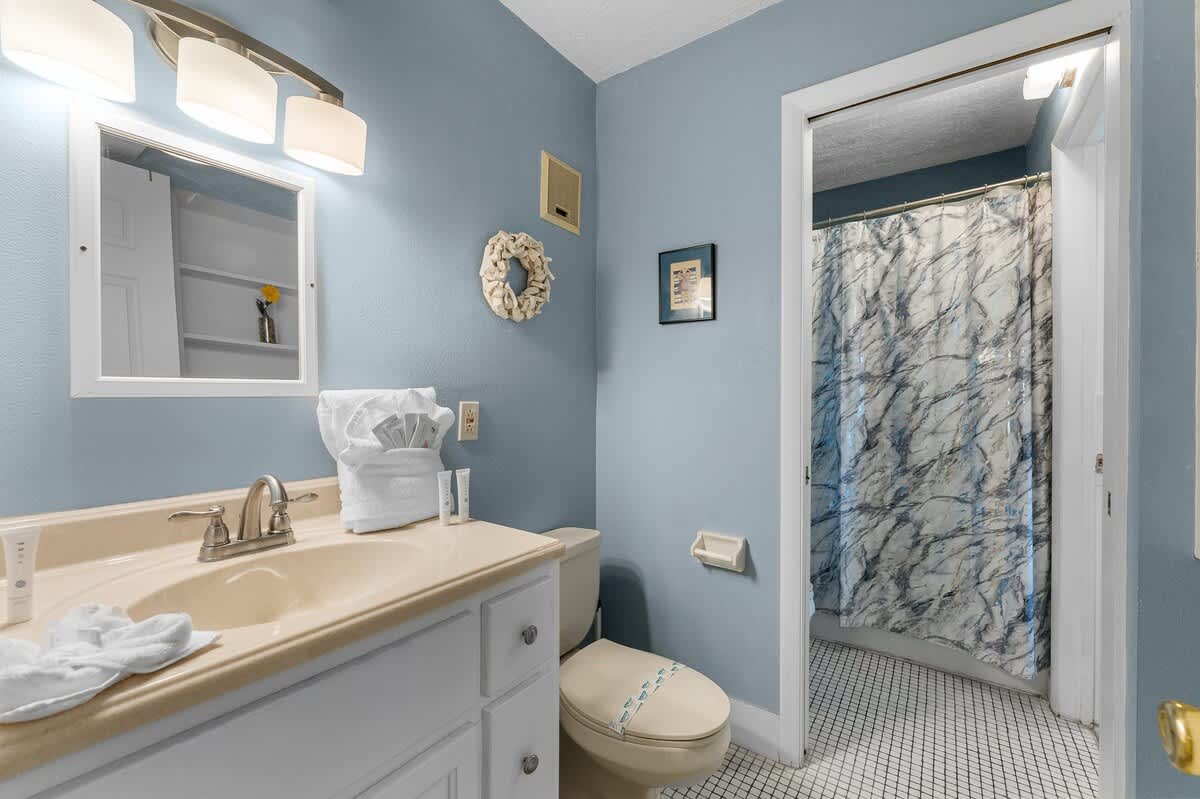The Summit 726 – Blue bathroom with sink, mirror, toilet, and shower curtain; decorative items and toiletries visible.