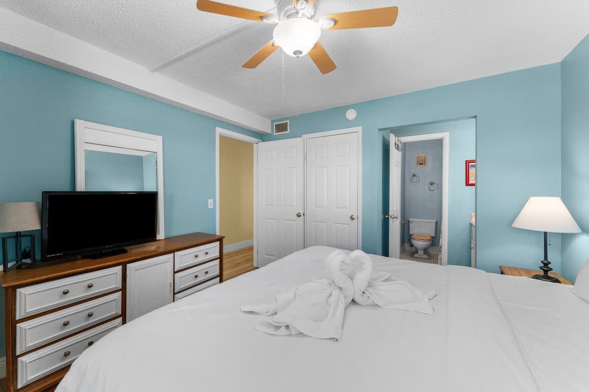 The Summit 726 – Cozy bedroom with a ceiling fan, TV, and bathroom door in view.