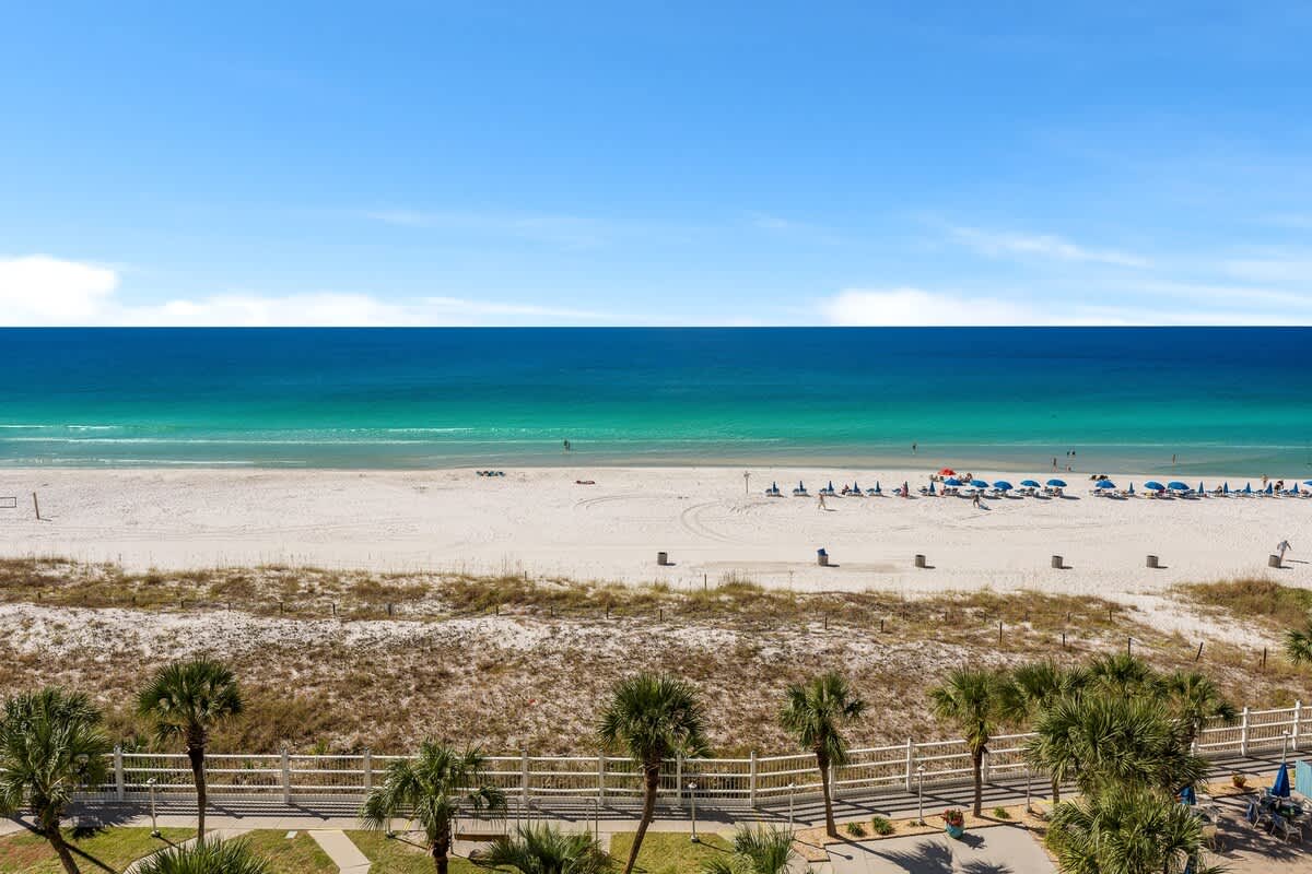The Summit 726 – Ocean view from balcony with sandy beach, umbrellas, and palm trees in foreground.