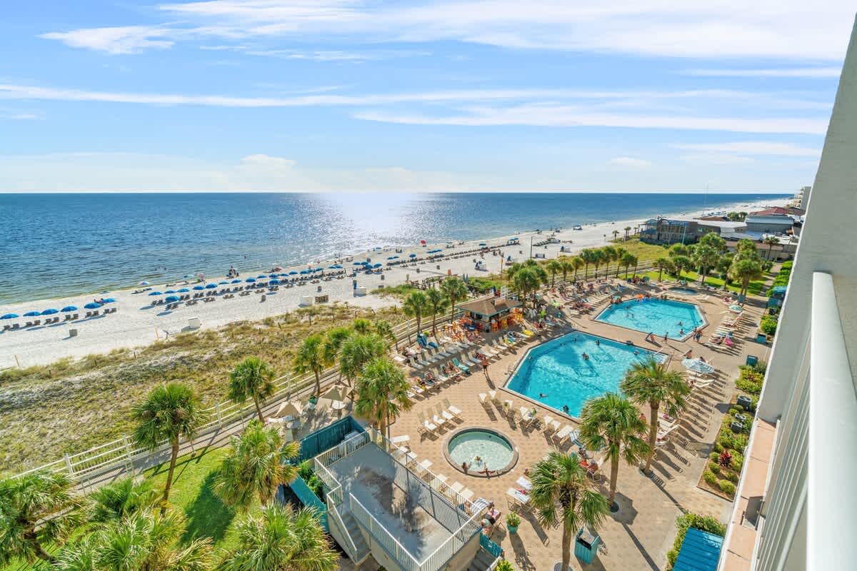 The Summit 726 – Aerial view of two swimming pools, hot tub, beach, and ocean with sun loungers and umbrellas.