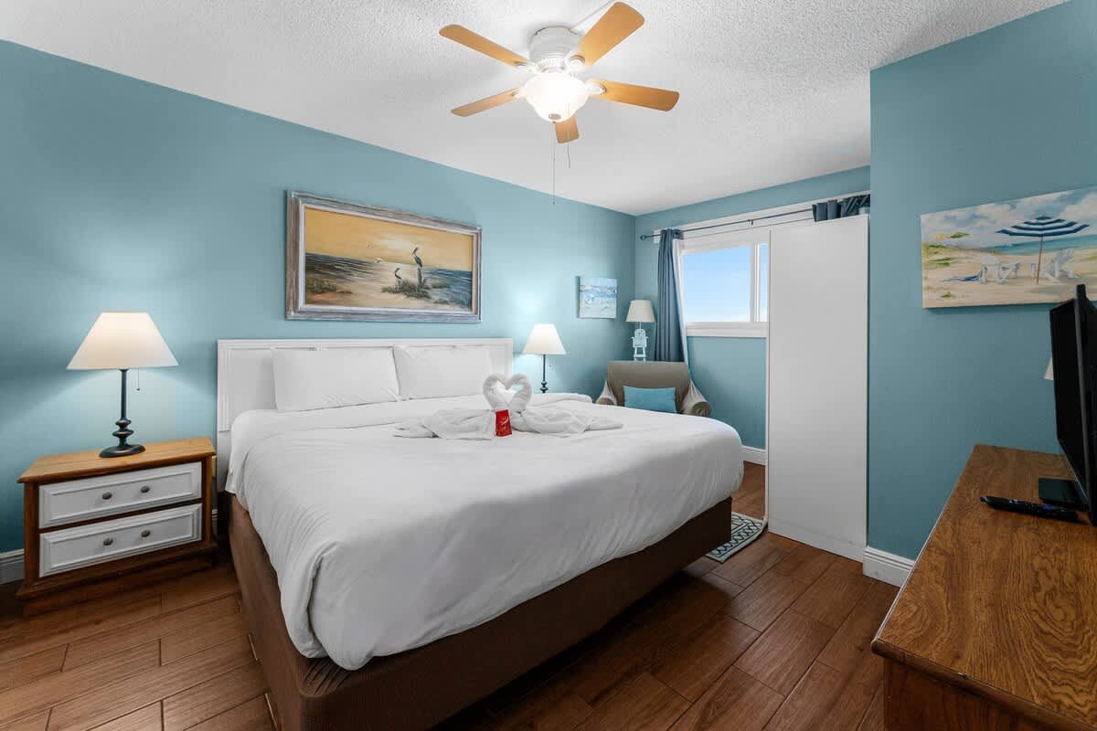 The Summit 726 – Cozy bedroom with a queen bed, armchair, TV, and blue walls. Window view of the sky.