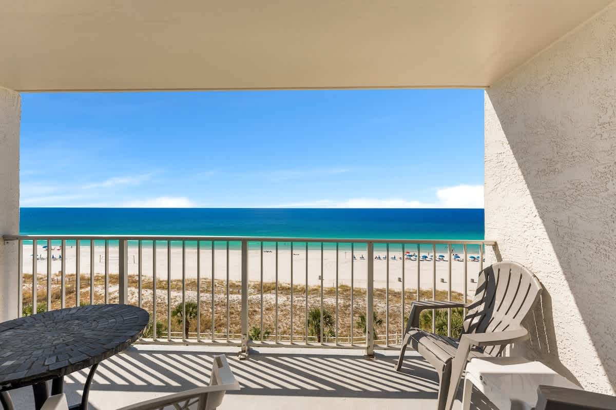 The Summit 726 – Balcony view of ocean, beach, and chairs beneath a clear blue sky.
