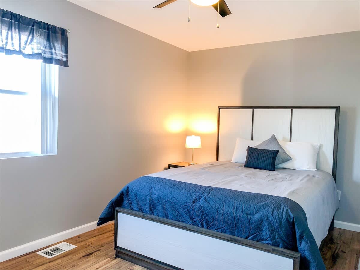 5218 Beach Dr B – Cozy bedroom featuring a queen bed, nightstand, lamp, and window with sheer curtains.