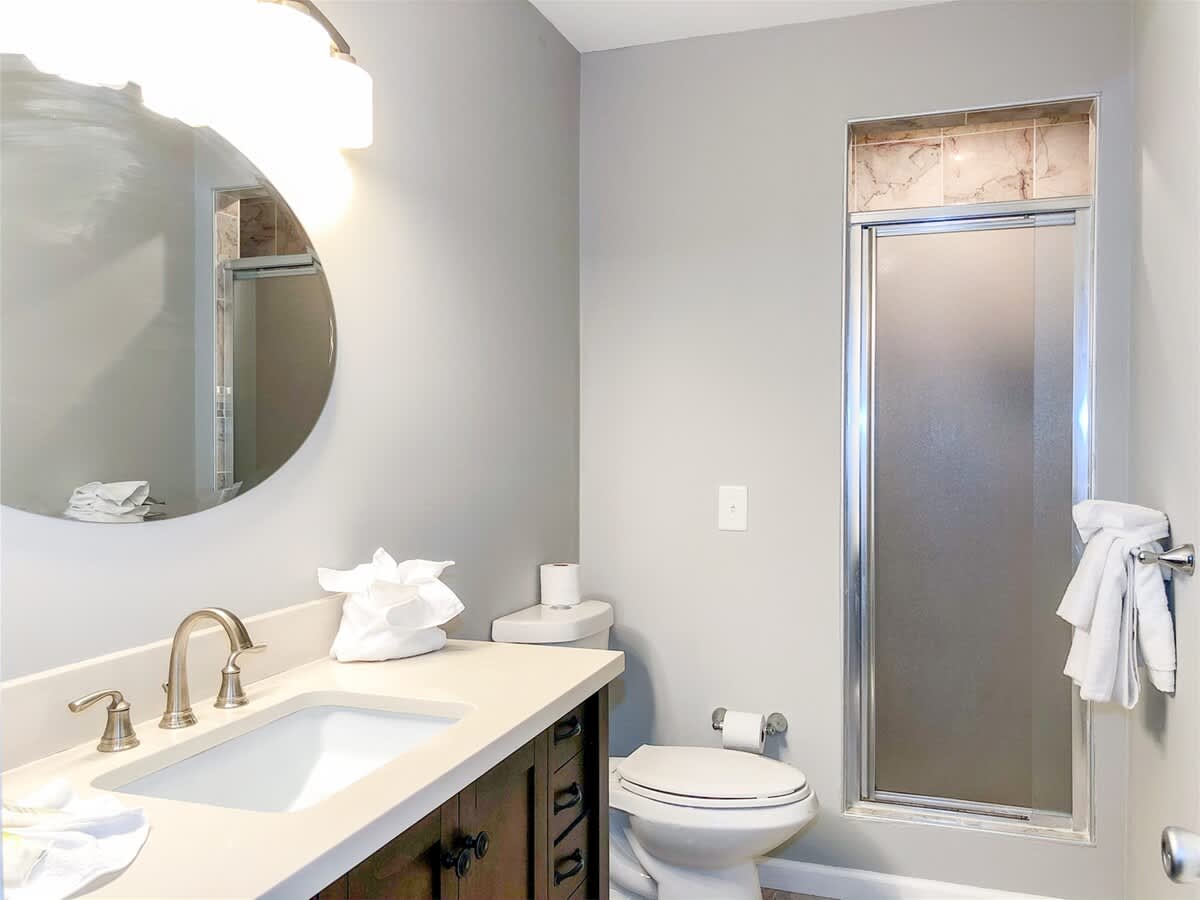 5218 Beach Dr B – Bathroom featuring a sink, toilet, shower, and lighted mirror with gray walls.