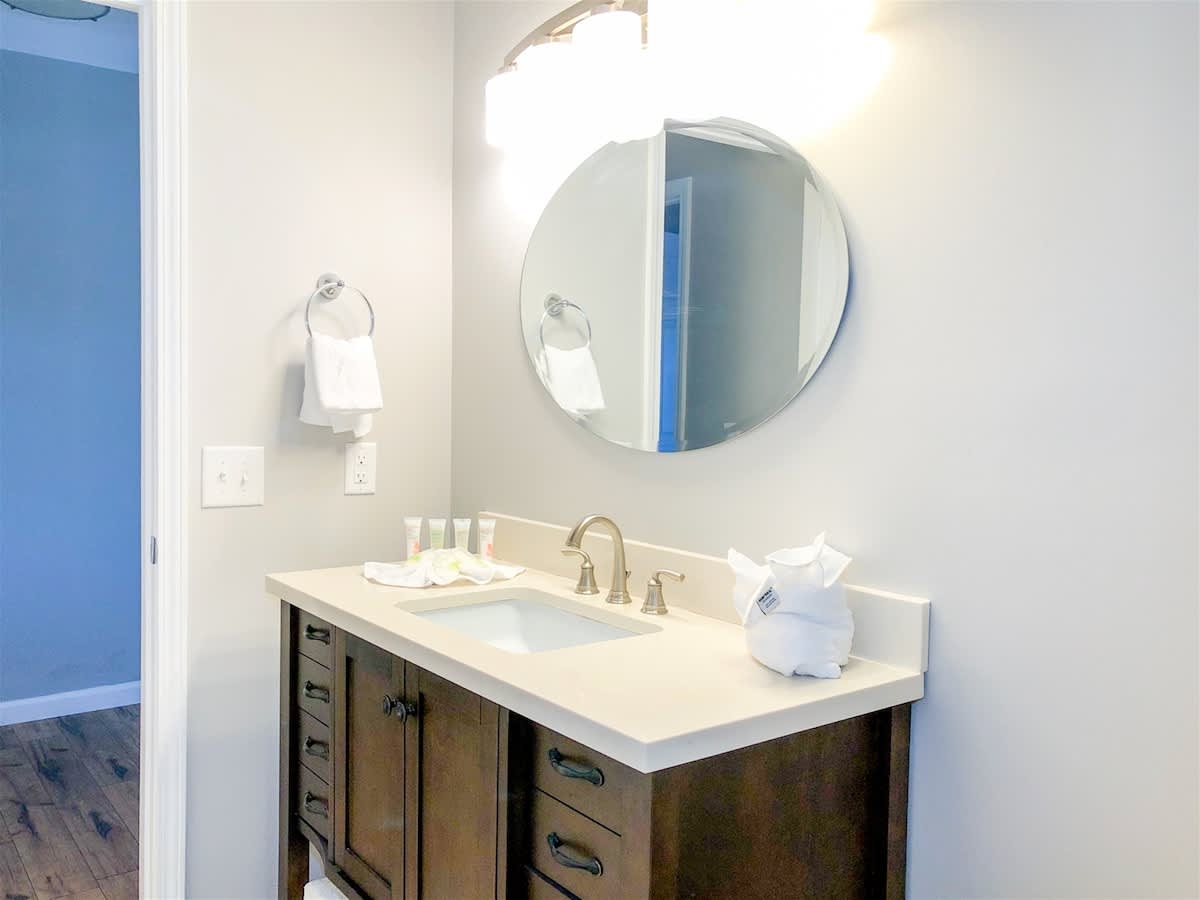 5218 Beach Dr B – Modern bathroom with a circular mirror, countertop sink, and wooden cabinet. Towels and toiletries visible.