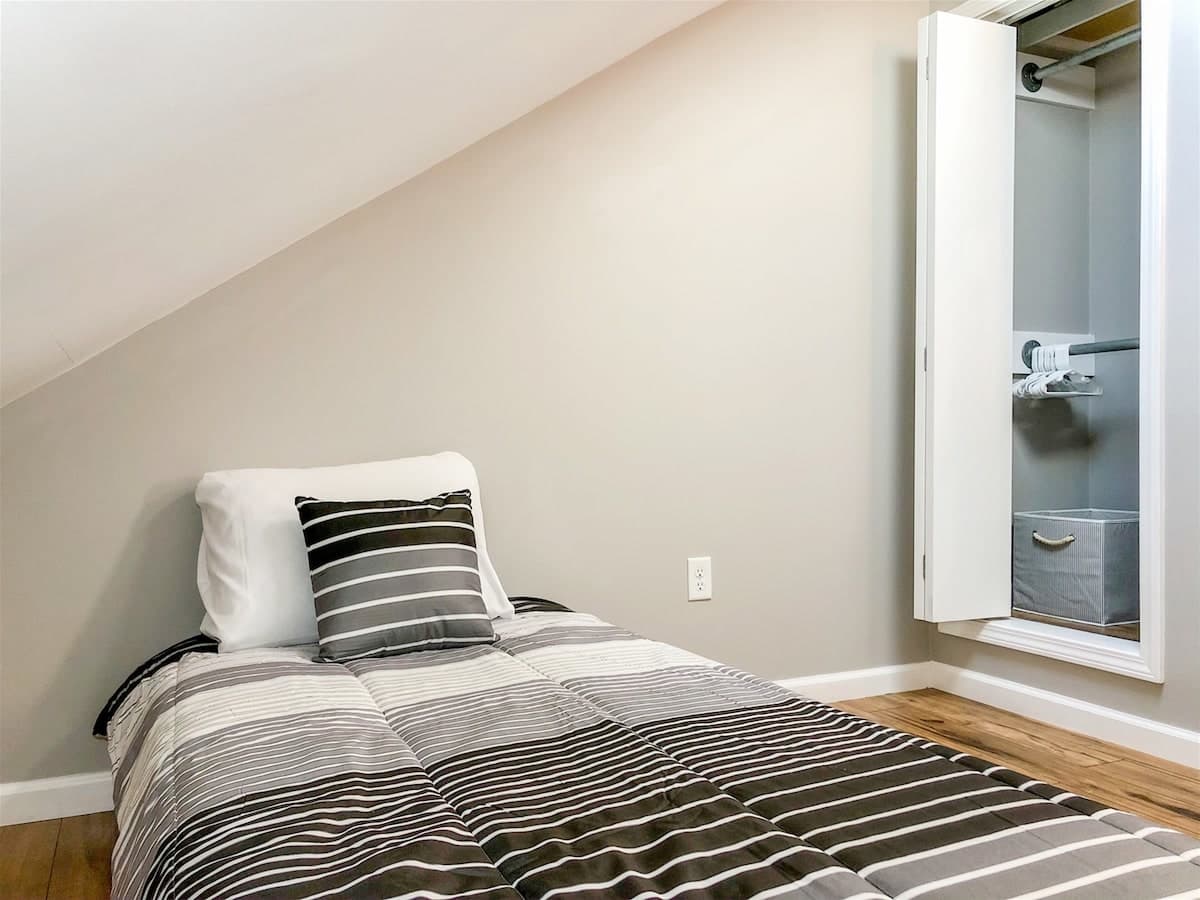 5218 Beach Dr B – Small bedroom with a single bed, striped bedding, and open closet.
