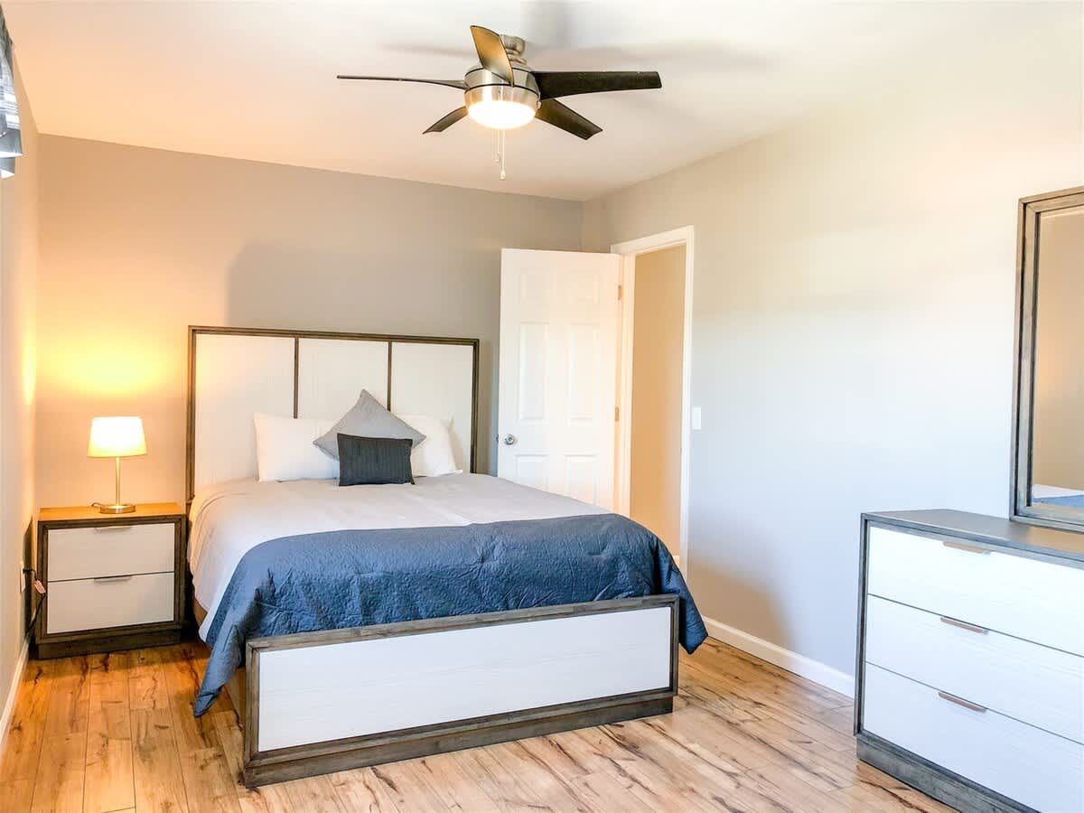 5218 Beach Dr B – Bright bedroom with a bed, nightstand, dresser, and ceiling fan.