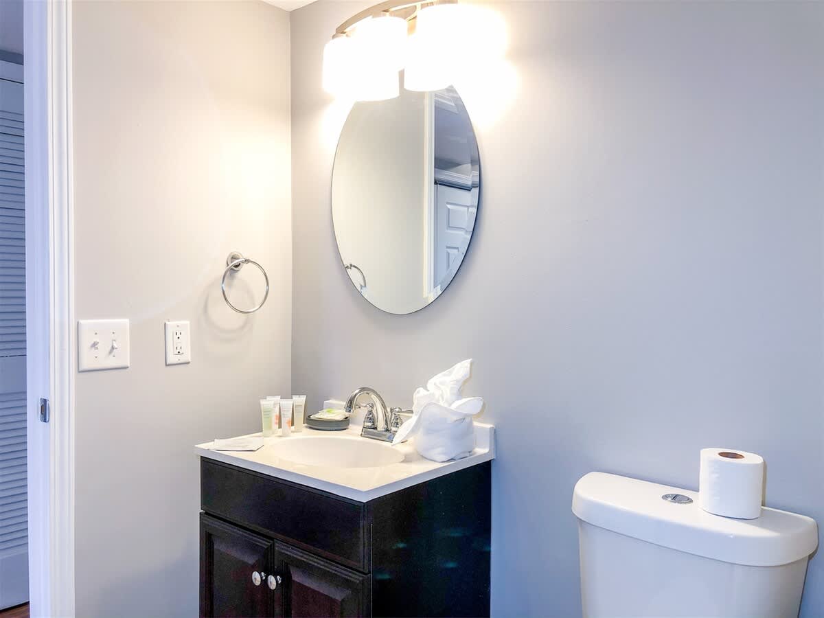5218 Beach Dr B – Small bathroom with a round mirror, sink, toilet, and toiletries on the counter.