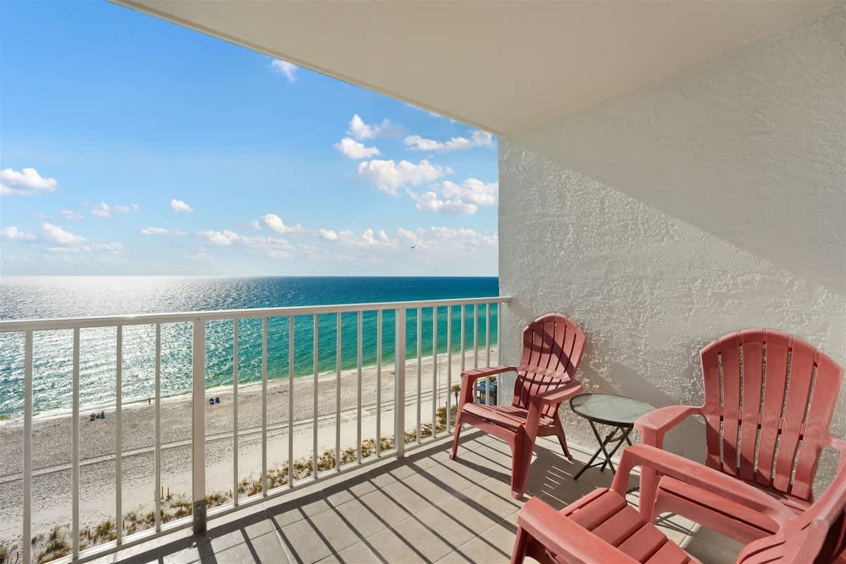 The Summit 1006 – Balcony with two red chairs and a table overlooking the beach and ocean.