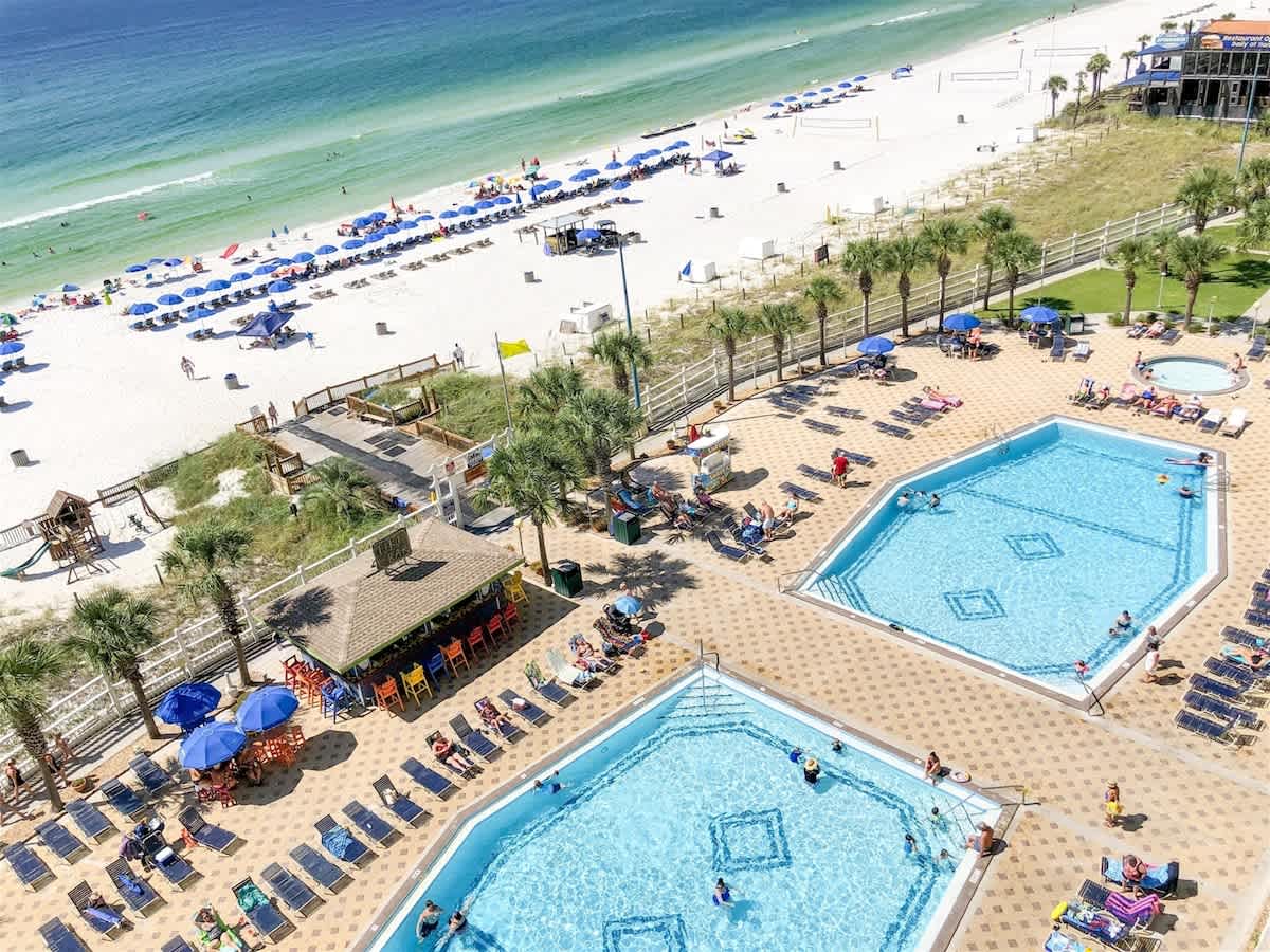 The Summit 1006 – Two swimming pools surrounded by lounge chairs, colorful umbrellas, and a view of the beach and ocean.