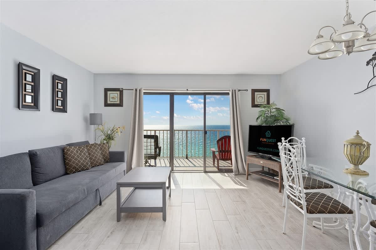 The Summit 1006 – Living room with ocean view, gray sofa, dining table, and sliding glass doors to the balcony.
