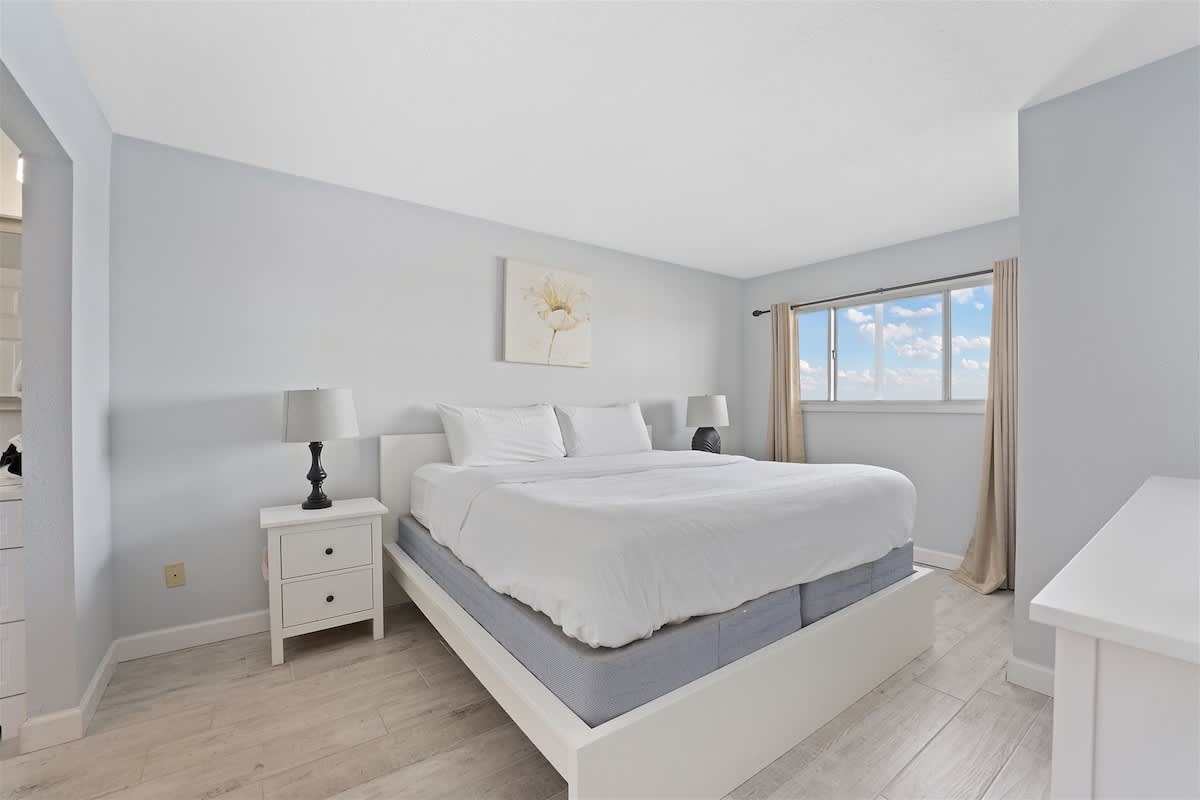 The Summit 1006 – Bright bedroom with a large bed, nightstands, and a window showcasing a view of clouds.