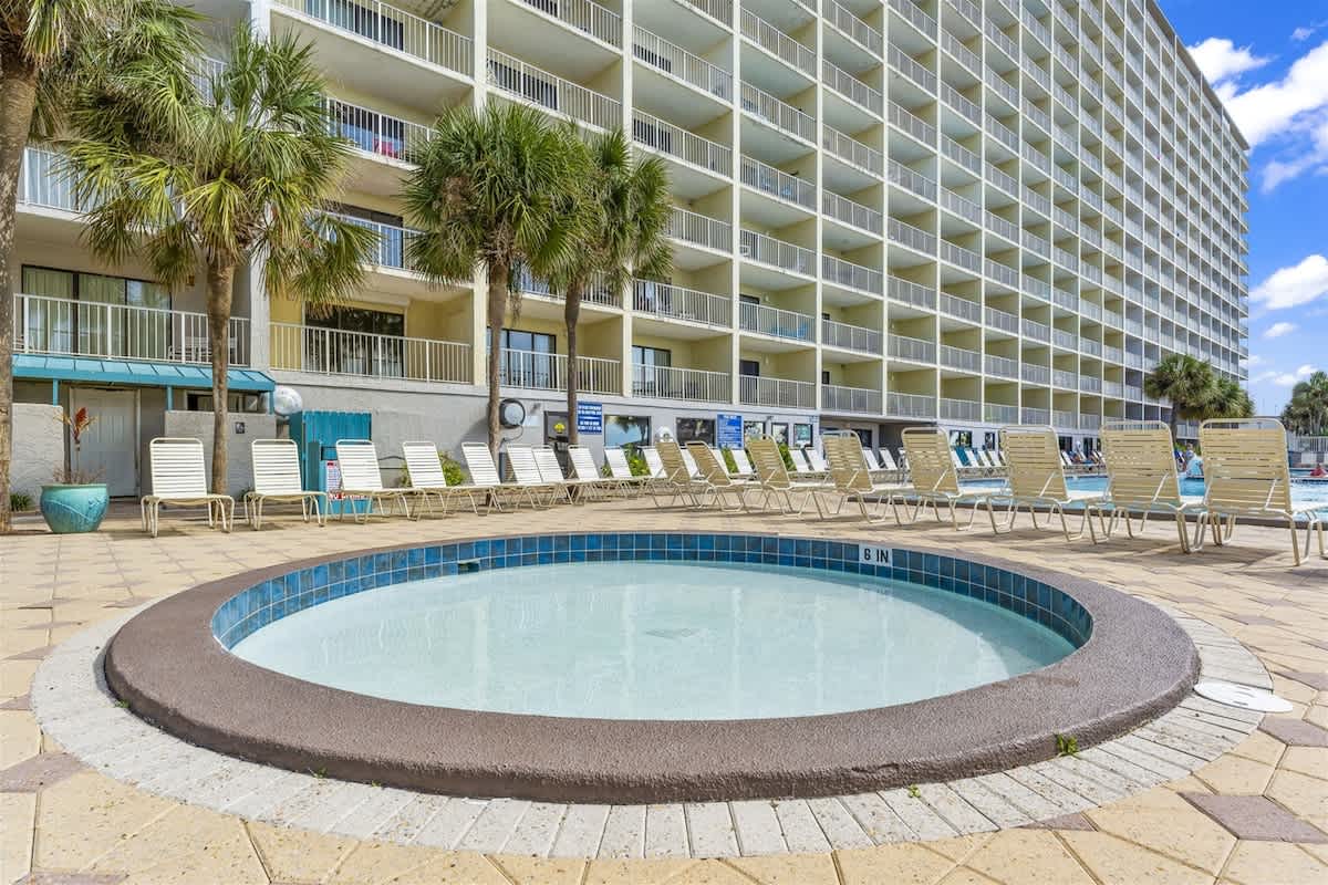 The Summit 1006 – Hot tub in a pool area surrounded by lounge chairs and palm trees.