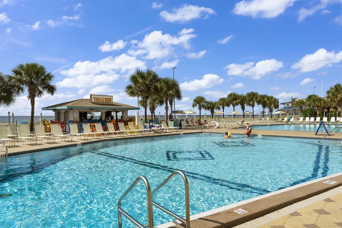 The Summit 1006 – Swimming pool area with a tiki bar, loungers, and a view of palm trees and sky.