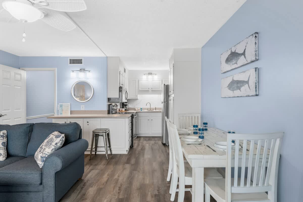The Summit 1031 – Bright open-plan living area with kitchen, dining table, and seating, featuring light blue walls and modern fixtures.