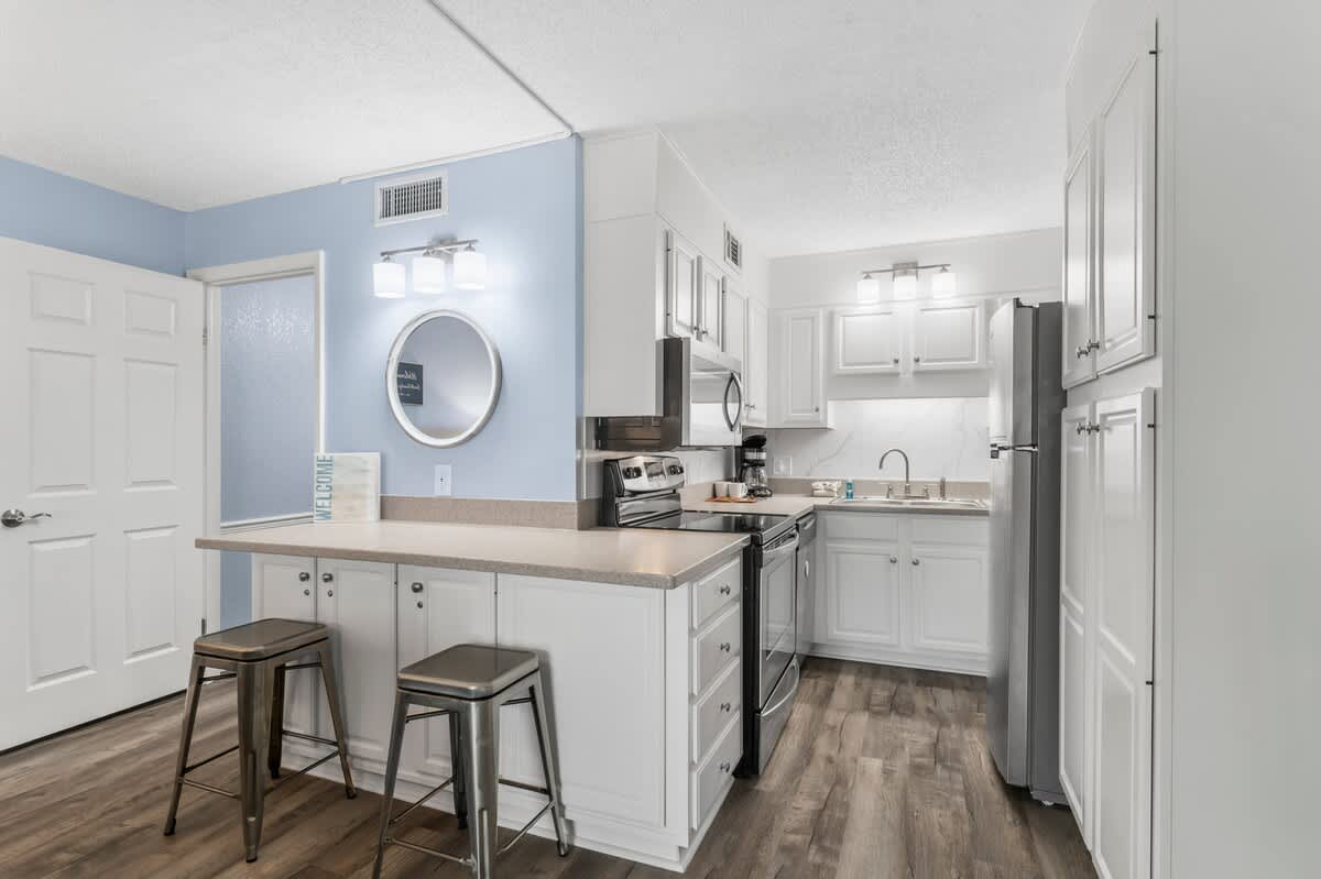 The Summit 1031 – Modern kitchen with white cabinetry, stainless steel appliances, and bar seating with two stools.
