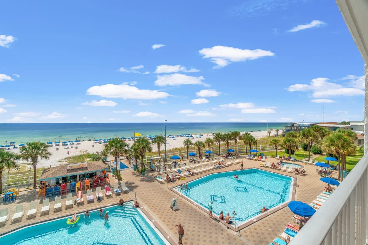 The Summit 1031 – Pool area with lounge chairs, tiki bar, and beach view under a clear blue sky.