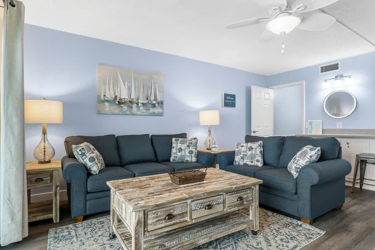 The Summit 1031 – Cozy living room with blue walls, two sofas, coffee table, and artwork featuring sailboats.
