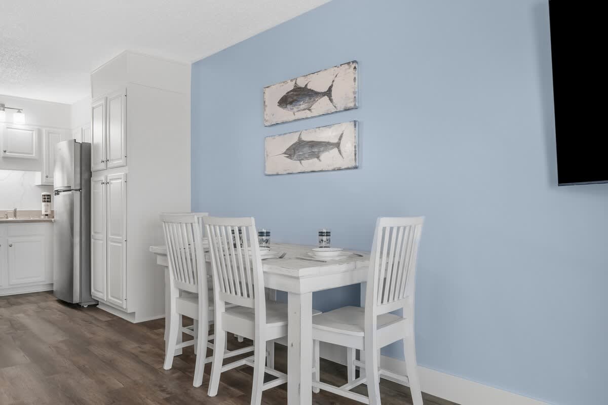 The Summit 1031 – Bright dining area with white furniture, blue wall, and fish-themed artwork, adjacent to a kitchen.