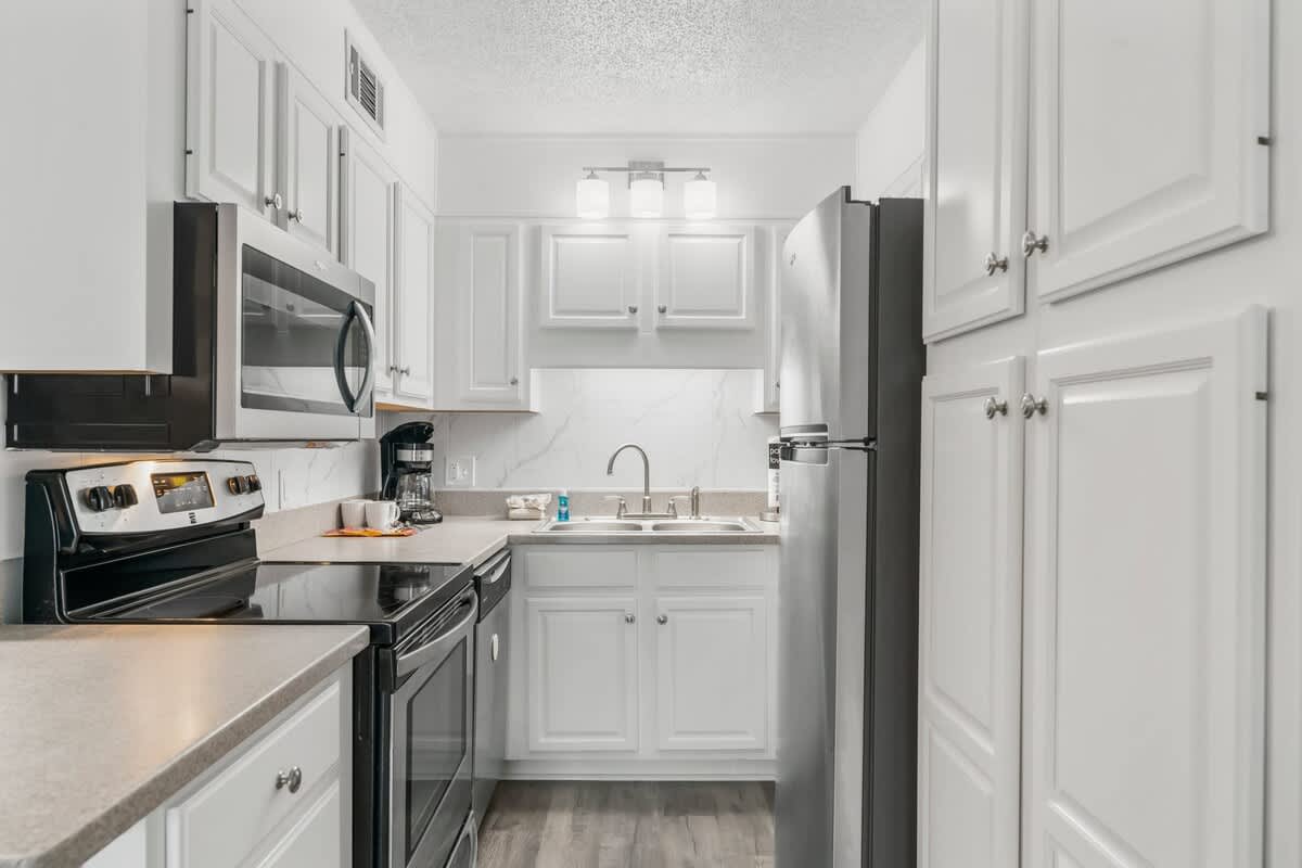 The Summit 1031 – Modern kitchen with white cabinets, stainless steel appliances, and a marble backsplash.