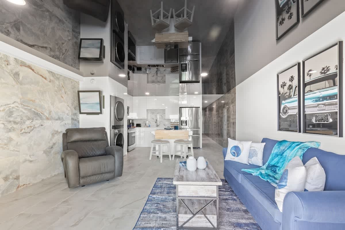 The Summit 306 – Living room with blue sofa, coffee table, kitchen area, and modern appliances.