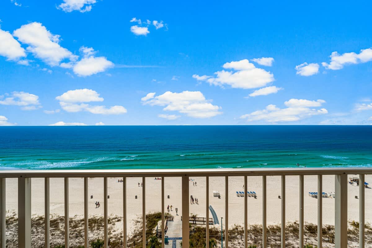 The Summit 1116 – Beachfront view from a balcony, showcasing sandy beach, ocean waves, and blue sky with clouds.