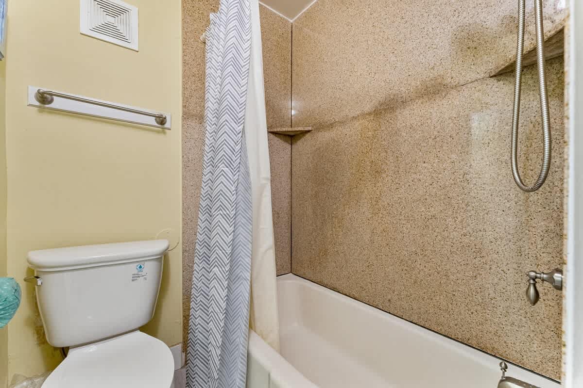 The Summit 1116 – Bathroom featuring a toilet, bathtub, and a shower with a patterned curtain.