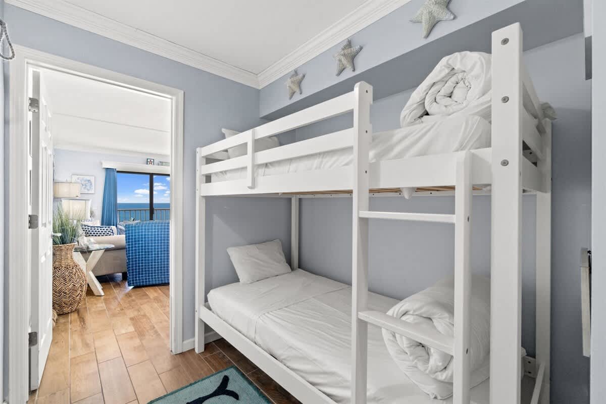 The Summit 502 – Bunk bed room with light blue walls, hardwood floor, and view of living area through open door.