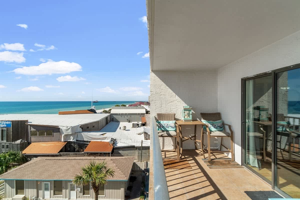 The Summit 502 – Balcony view of the ocean with two chairs and a small table, overlooking rooftops and palm trees.