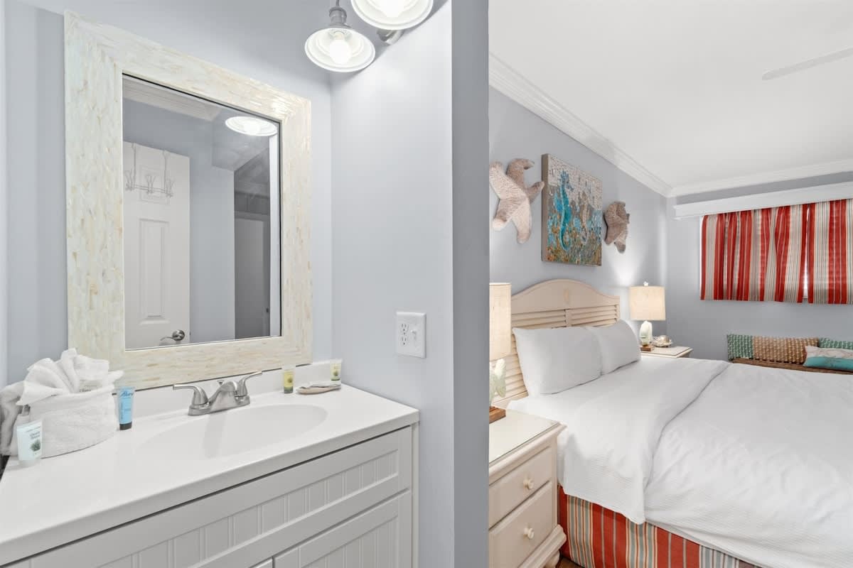 The Summit 502 – Cozy bedroom with a bed, nightstands, and adjoining bathroom featuring a mirror and sink.