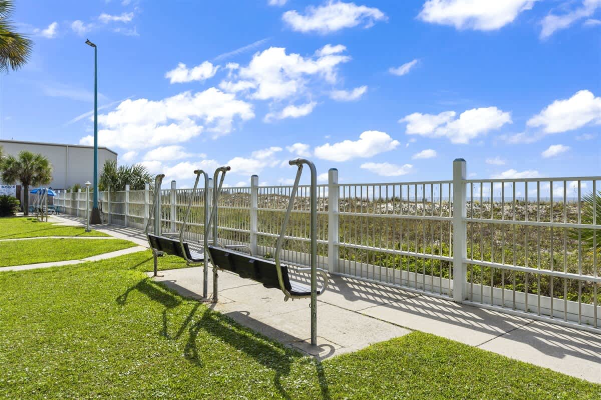The Summit 502 – Outdoor area with swings, grassy lawn, and a view of the beach and blue sky.