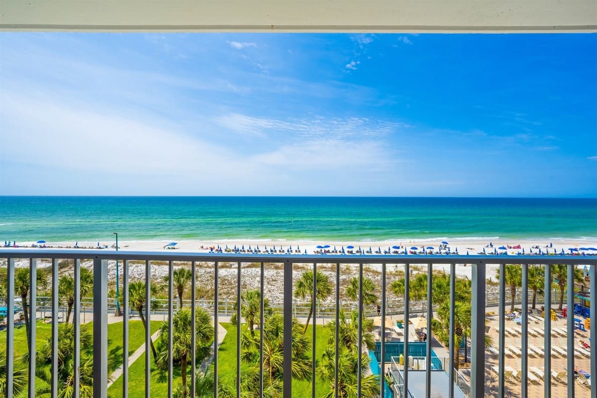 The Summit 626 – Ocean view from a balcony, overlooking beach, palm trees, and sun loungers on the sand.
