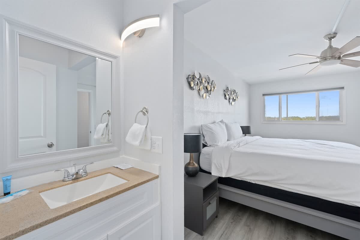 The Summit 626 – Bright bedroom with a king bed, dresser, and adjacent bathroom featuring a sink and large mirror.