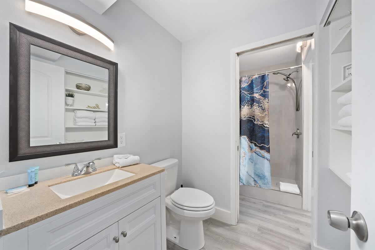 The Summit 626 – Modern bathroom featuring a vanity, mirror, shower with curtain, and storage shelves with towels.