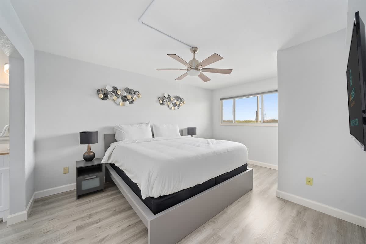 The Summit 626 – Modern bedroom with a large bed, ceiling fan, and windows offering natural light.