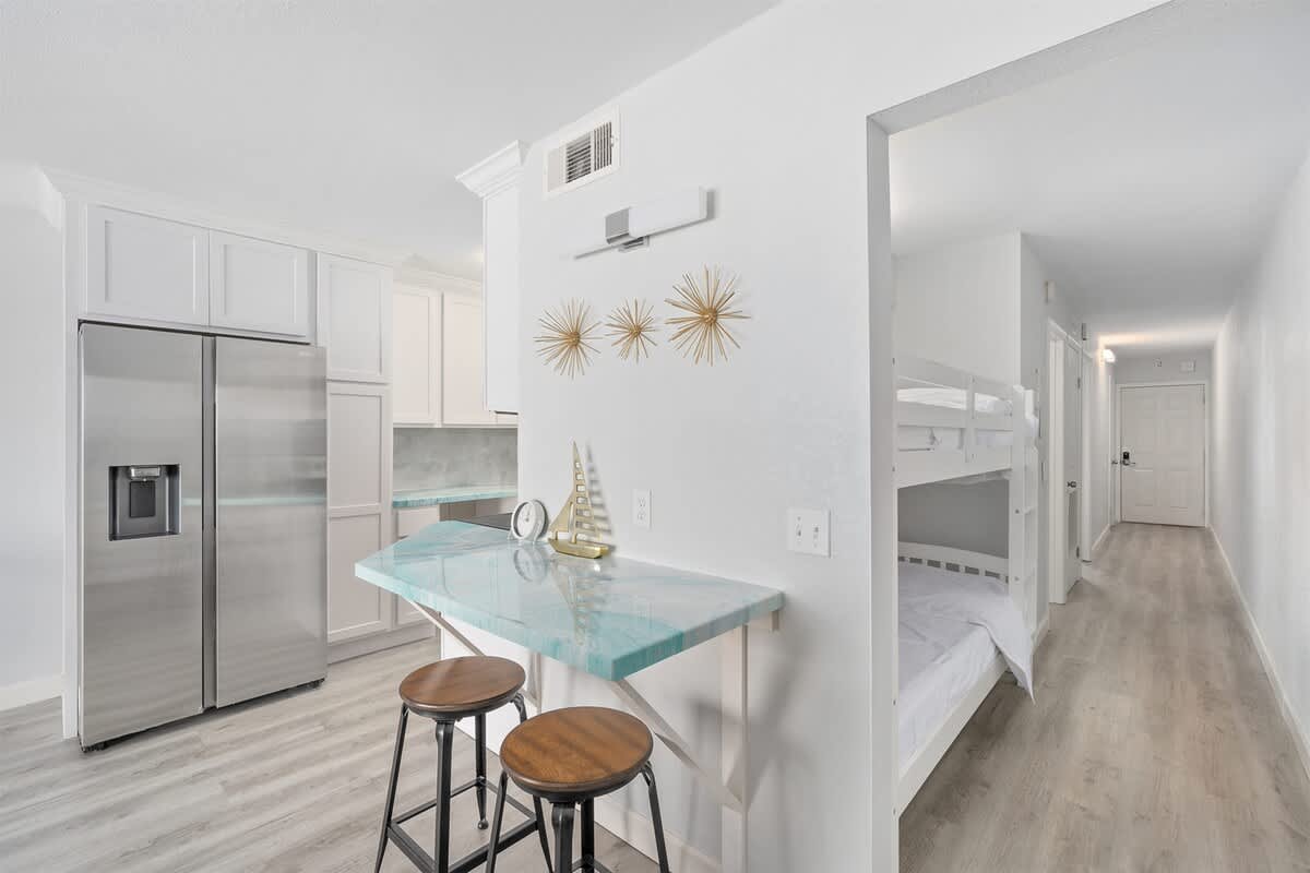 The Summit 626 – Modern studio kitchen with bunk beds, bar seating, and light wood flooring.