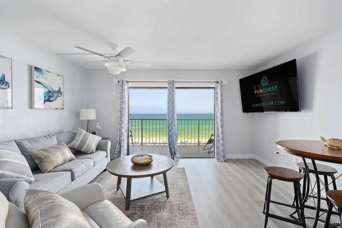 The Summit 626 – Living room with gray furniture, balcony view of the ocean, and a mounted TV.