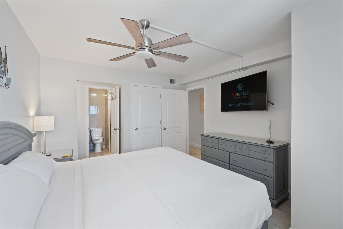 The Summit 615 – Bedroom with a king bed, ceiling fan, TV, and attached bathroom visible.
