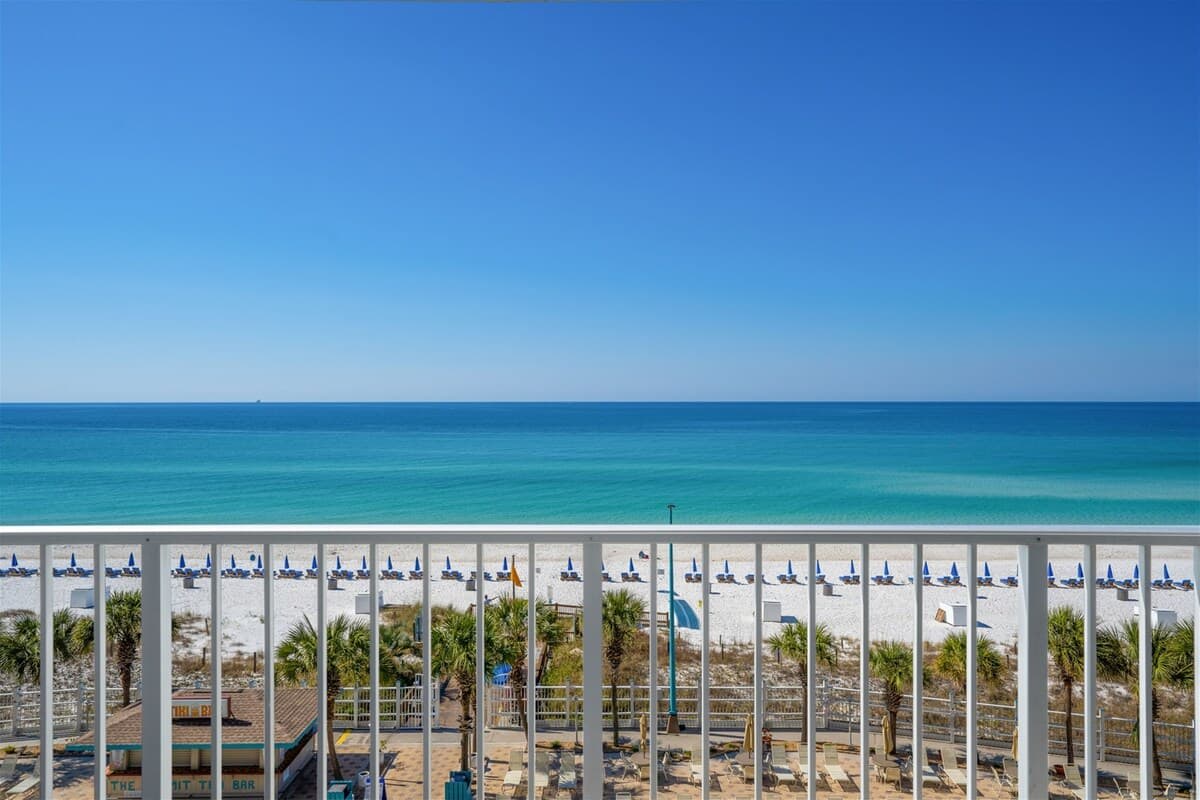 The Summit 615 – View from balcony showcasing ocean, beach chairs, and palm trees with a clear blue sky.