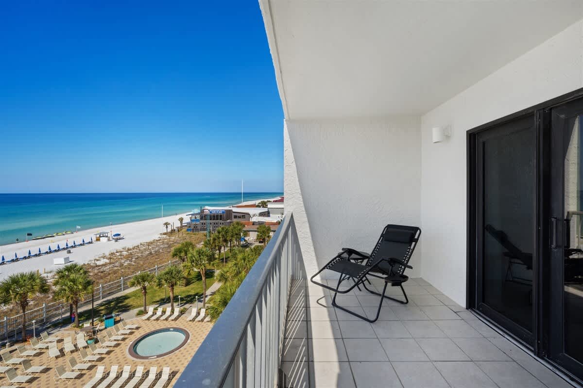 The Summit 615 – Balcony view of ocean, beach, and pool area with two black lounge chairs.