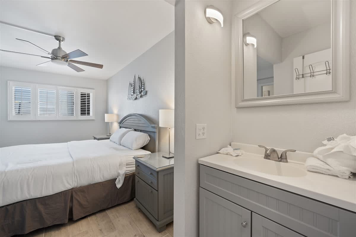 The Summit 615 – Bright bedroom with a bed, nightstand, and nearby bathroom vanity with sink and mirror.