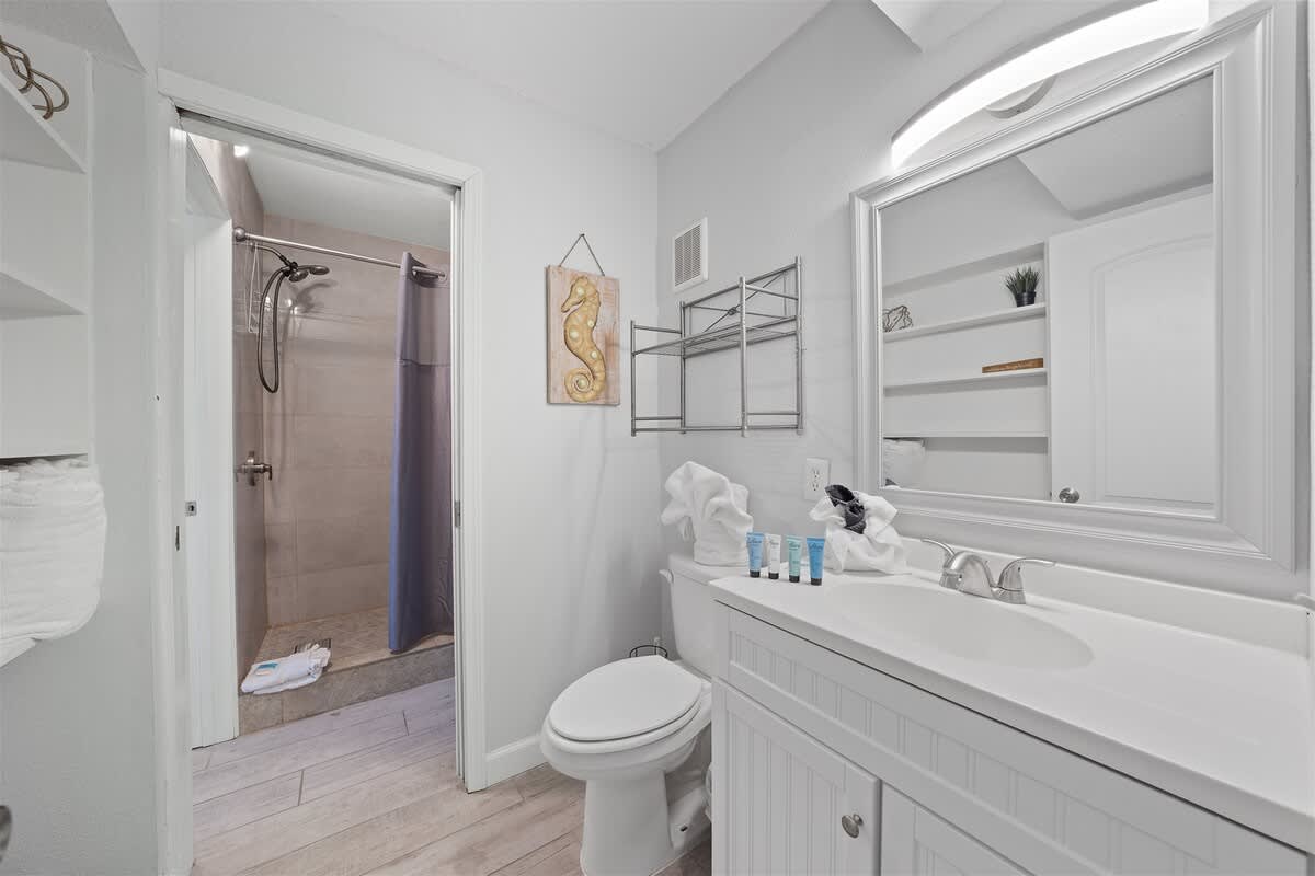 The Summit 615 – Bright bathroom with shower, white vanity, mirror, and shelving for towels and toiletries.