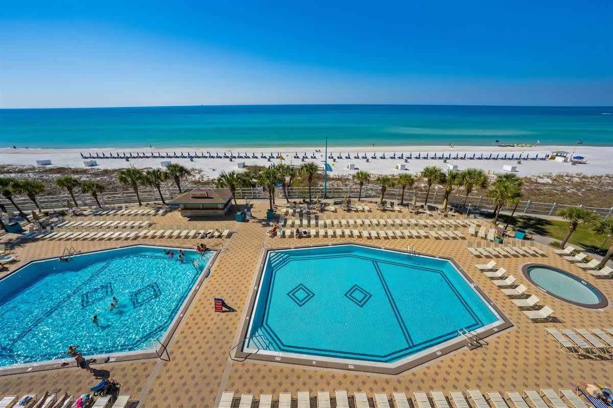 The Summit 615 – View of pools and beach, with palm trees and lounge chairs under clear blue skies.